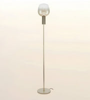 A modern floor lamp with a slim metallic pole, a round base, and a frosted glass shade on a plain light beige background.