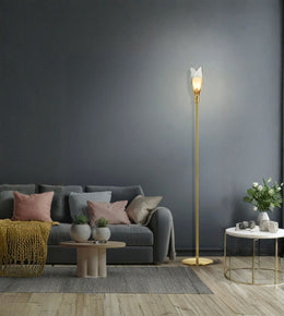 A modern gold floor lamp with a sculptural white leaf-shaped shade stands in a styled living room next to a gray sofa and a small white side table.