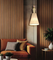 A warm, modern living room scene featuring a brown leather sofa with patterned and solid throw pillows, a brown slatted accent wall, a hanging pendant light with a beige shade, and a side table with a potted plant.