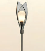 A modern tulip-shaped floor lamp with a glowing warm bulb inside a smoky translucent glass shade, mounted on a dark metal pole against a plain light beige background.