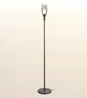 A modern floor lamp with a tall black metal pole, a round base, and a sculptural openwork shade at the top holding a glowing light bulb, set against a soft beige gradient background.