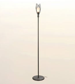 A modern floor lamp with a tall black metal pole, a round base, and a sculptural openwork shade at the top holding a glowing light bulb, set against a soft beige gradient background.