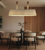 A modern dining room scene featuring a large rectangular pendant light with a beige linen shade hanging above a glass-top dining table and six upholstered chairs with beige seats and black legs. The background includes a warm wood slat wall panel.
