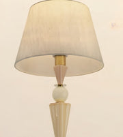 A table lamp with a tapered beige fabric shade, a cream-colored faceted base, a white spherical accent, and a gold-toned metal connector, shown against a plain light background.