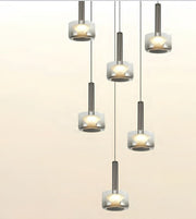 Five modern pendant lights with brushed silver cylindrical shades and frosted glass shades, arranged in a staggered vertical layout against a light beige background.