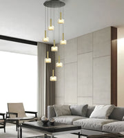 A modern multi-light pendant chandelier with six cylindrical glass shades and brushed brass rods, suspended from a circular ceiling mount in a contemporary living room setting.