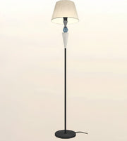 A modern floor lamp with a black metal stand, a round base, a tapered beige fabric shade, and decorative glass accents in the center.