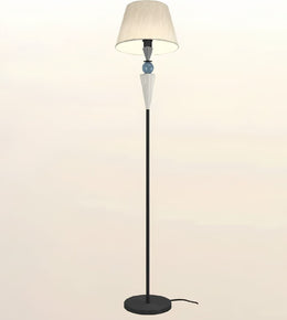 A modern floor lamp with a black metal stand, a round base, a tapered beige fabric shade, and decorative glass accents in the center.