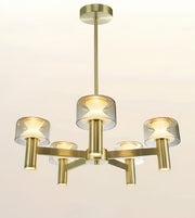 A modern five-light chandelier with a brushed gold/brass metal frame and clear glass cylindrical shades, shown against a plain off-white background.