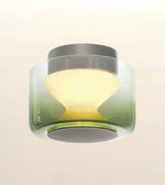 A modern flush-mount ceiling light fixture with a translucent green-to-clear gradient glass shade, a gray top canopy, and a warm yellow illuminated diffuser, shown against a plain off-white background.
