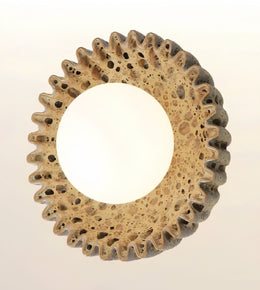 A circular decorative wall mirror with a textured, porous frame resembling travertine stone, featuring a wide white reflective center and a scalloped outer edge.