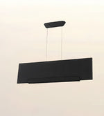 A modern rectangular black pendant light with a subtle herringbone texture, suspended by two thin cables from a matching curved ceiling mount against a plain off-white background.