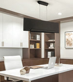 A modern rectangular black pendant light with a textured chevron pattern hangs over a white desk in a contemporary home office setting with brown shelving and white cabinets.