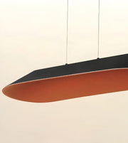 A modern pendant light with a curved, elongated design, featuring a matte black top surface and a terracotta orange underside, suspended by thin cables against a plain off-white background.