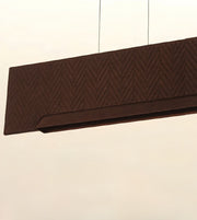 A close-up of a dark brown rectangular pendant light fixture with a textured chevron pattern, suspended by thin cables against a plain off-white background.