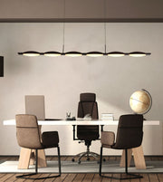 A modern office interior with a long linear pendant light hanging above a white desk, flanked by three upholstered office chairs. A laptop, books, and a globe sit on the desk against a light neutral wall.