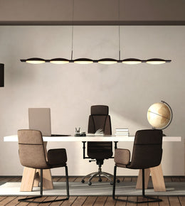 A modern office interior with a long linear pendant light hanging above a white desk, flanked by three upholstered office chairs. A laptop, books, and a globe sit on the desk against a light neutral wall.