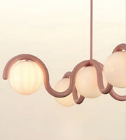 A modern pendant light fixture with a wavy, flowing frame in a muted dusty rose color and three frosted glass globes, shown against a plain off-white background.