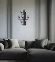 A modern multi-arm wall sconce with frosted glass globes mounted on a light gray paneled wall above a dark gray sectional sofa with matching pillows.