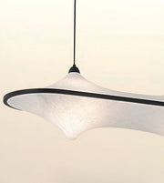 A modern pendant light with a wide, organic-shaped white textured shade and a black rim, suspended by a thin black cord against a warm off-white background.