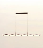 A modern linear chandelier with six illuminated oval light heads and a dark metal frame, suspended by two thin cables from a rectangular ceiling mount against a plain off-white background.