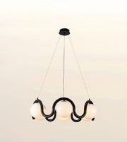 A modern multi-light pendant chandelier with a black wavy metal frame and five glowing white spherical glass shades, suspended from a ceiling canopy against a plain light background.