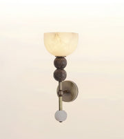 A wall-mounted sconce with a frosted glass dome shade, two dark textured spherical accents, a brass-toned vertical stem, and a round white glass finial, shown against a soft off-white background.