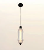 A modern cylindrical pendant light with a ribbed clear glass shade, a warm glowing bulb inside, and black metal hardware, suspended against a soft beige gradient background.