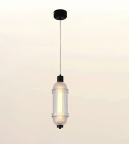 A modern cylindrical pendant light with a ribbed clear glass shade, a warm glowing bulb inside, and black metal hardware, suspended against a soft beige gradient background.