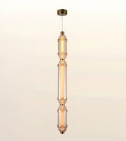 A modern vertical pendant light fixture with three stacked cylindrical glass shades in a warm frosted amber tone, accented by brass-toned metal hardware and a matching ceiling canopy, shown against a plain off-white background.