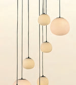 Modern multi-light pendant fixture with six matte frosted glass globes suspended by thin black cords against a warm off-white background.