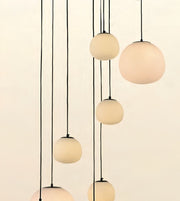 Modern multi-light pendant fixture with six matte frosted glass globes suspended by thin black cords against a warm off-white background.