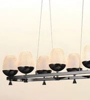 Modern linear chandelier with six textured frosted glass dome shades and black metal bowls, suspended against a plain light background.