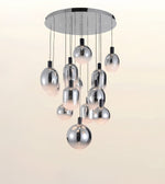 A modern multi-light chandelier with a circular chrome ceiling canopy and multiple hanging polished metal globe shades, shown against a plain light beige background.