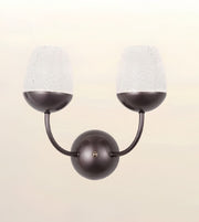 A modern two-light wall sconce with a matte dark bronze finish and textured white glass shades, shown against a soft beige gradient background.