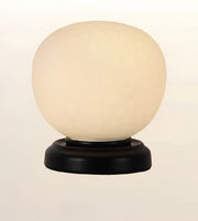 A table lamp with a large, rounded, frosted off-white glass globe shade on a round, dark brown wooden base, set against a plain light background.