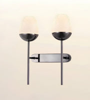 A modern double-light wall sconce with a glossy black metal frame, featuring two textured frosted glass shades and a rectangular backplate, shown against a plain off-white background.