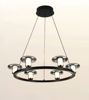 A modern multi-light ring chandelier with a matte black circular frame, silver-toned metal shades, and glowing warm white bulbs, suspended by thin black cords from a round ceiling canopy against a plain light background.