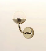 A modern wall-mounted sconce with a brushed brass/gold metal base, curved arm, and textured white glass globe shade, shown against a plain light beige background.