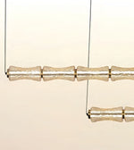 A modern multi-light linear chandelier with textured, translucent glass cylindrical shades suspended by thin black wires against a warm cream background.