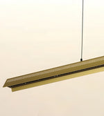 A modern linear pendant light fixture in a brushed brass or gold finish, suspended by a thin black cord against a plain off-white background.