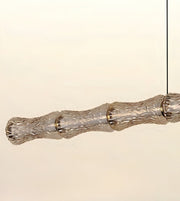 A modern horizontal pendant light with a textured, segmented glass shade suspended by a thin black cord against a plain off-white background.