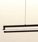 A modern linear LED pendant light fixture in matte black, suspended by a thin black cable against a warm off-white background.