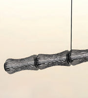 A modern pendant light fixture with a segmented, textured gray glass shade suspended by a thin black cord against a warm cream background.
