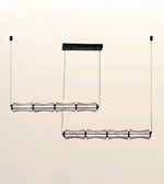 A modern multi-light linear pendant chandelier with textured clear glass shades and black metal hardware, shown suspended against a plain light beige background.