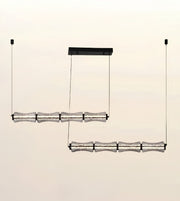 A modern multi-light linear pendant chandelier with textured clear glass shades and black metal hardware, shown suspended against a plain light beige background.