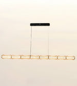 A modern linear pendant light fixture designed to resemble a segmented bamboo pole, featuring a warm gold-toned metallic finish and a sleek black ceiling canopy, suspended against a plain off-white background.