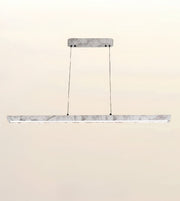 A modern linear LED pendant light with a white marble-look horizontal bar suspended by two thin black cables from a matching rectangular ceiling mount, shown against a plain beige background.