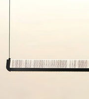 A modern linear pendant light suspended by a thin black cord, featuring a black frame and a textured white and gray striped diffuser panel.