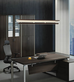 A modern office setup featuring a dark wood executive desk with a matching dark wood hutch, a black office chair, and a sleek rectangular pendant light hanging above the desk.